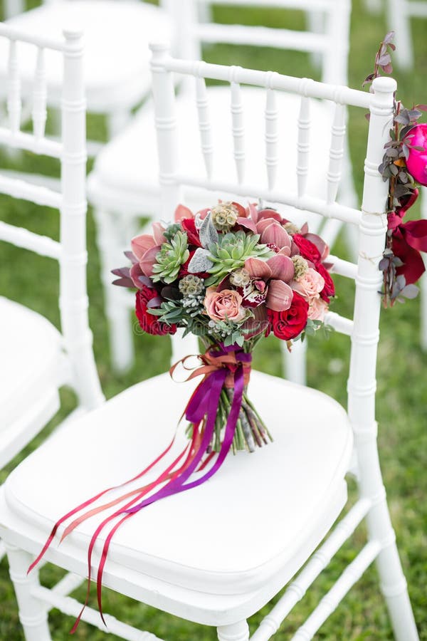 Stunning red bridal bouquet on white chair. Wedding ceremony. Mix of succulents, orchids and roses royalty free stock photography Stunning red bridal bouquet on white chair. Wedding ceremony. Mix of succulents, orchids and roses royalty free stock photography