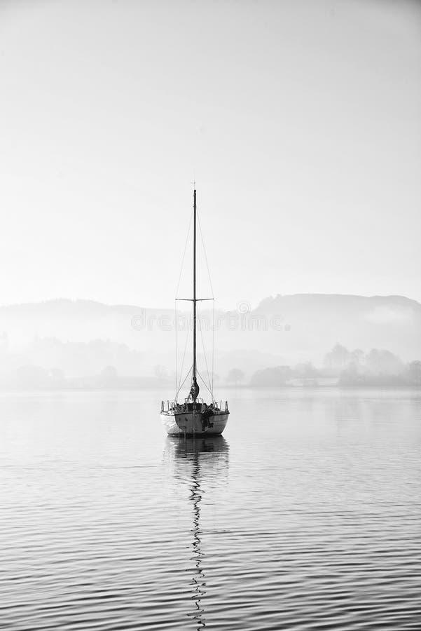 Stunning unplugged fine art landscape image of sailing yacht sitting still in calm lake water in Lake District during peaceful