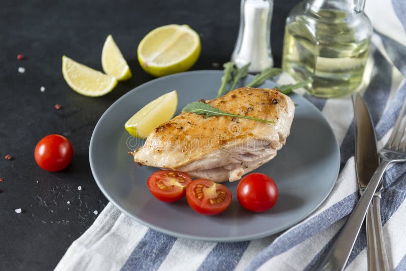 Stycke av stekt kycklingfilén med arugula, limefrukt och tomaten på en platta arkivbild Stycke av stekt kycklingfilén med arugula, limefrukt och tomaten på en platta arkivbild