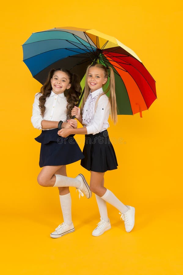Styl jesienny. szczęśliwe małe dziewczynki trzymające parasol w stylu tęczy na żółtym tle. małe dzieci uśmiechające się do szkoły zdjęcie stock