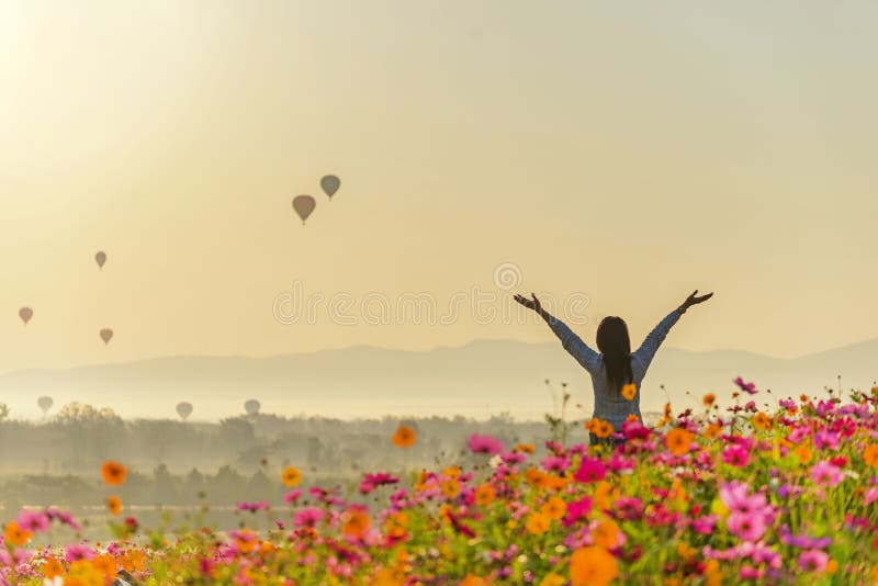 Lifestyle traveler woman raise hand feeling good relax and happy freedom and see the fire balloon on the nature tea and cosmos farm in the sunrise morning. Travel and summer Concept. Lifestyle traveler woman raise hand feeling good relax and happy freedom and see the fire balloon on the nature tea and cosmos farm in the sunrise morning. Travel and summer Concept