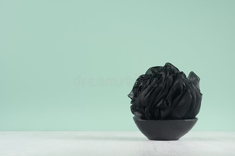 Style black accessorie for skin cleansing - bath sponge on black bowl on green mint menthe wall and white wood table.