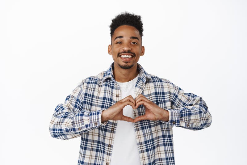 Stylish african american man smiling, showing heart on chest gesture, I love you, confess that he likes loves someone