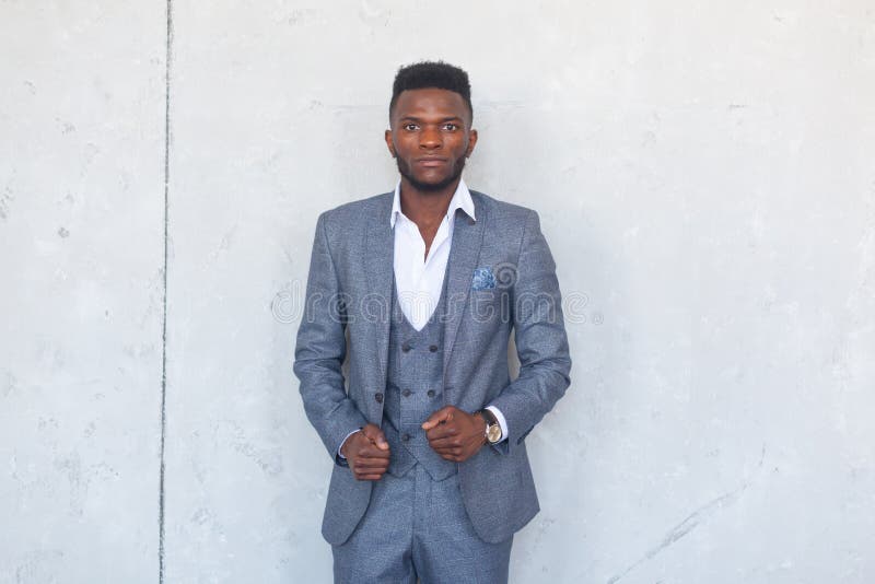 Stylish African black man is posing in three piece suit against a gray concrete wall