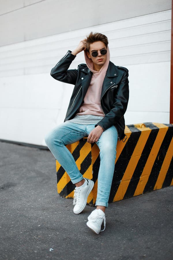 Premium Photo | Fashionable handsome young man hipster model in a stylish  outfit with leather jacket hoodie jeans and white sneakers sitting near a  brick wall