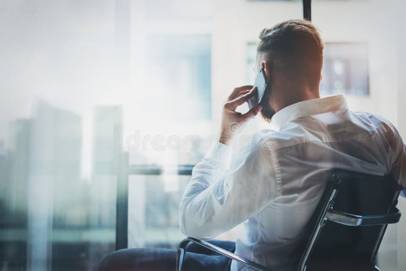 Stylish banker making mobile call at modern loft after work day.Man sitting in chair and looking out the panoramic stock photography Stylish banker making mobile call at modern loft after work day.Man sitting in chair and looking out the panoramic stock photography
