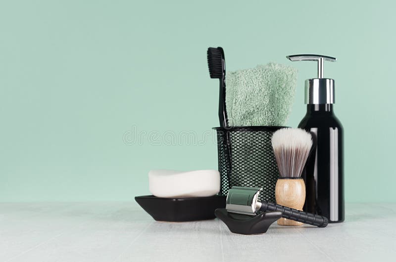 Stylish bathroom interior with black shaving accessories on green  wall, white table - razor, toothbrush, towel, soap, shave brush