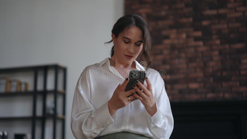 Stylish business woman holds a mobile phone in her hands, messenger chats with colleagues at work and speaks out loud. Smiling, while sitting in the office