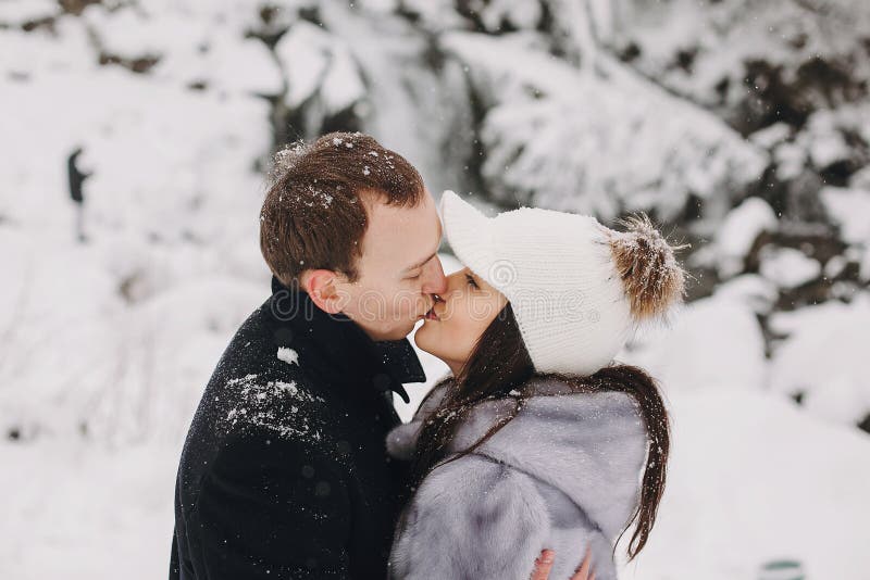 Stylish couple kissing in winter snowy mountains. Happy romantic