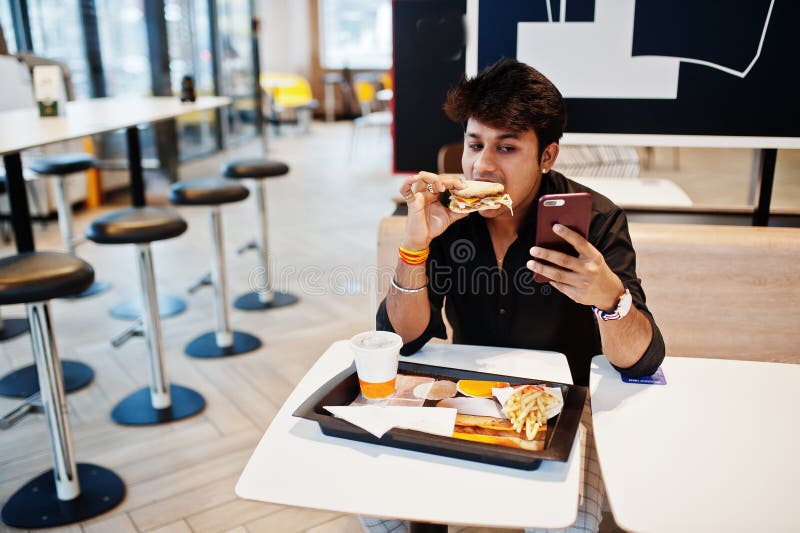 Stylish and Funny Indian Man Sitting at Fast Food Cafe and Eating Hamburger and Making Selfie by Phone Stock Image - Image of dish, cafe: 229221573 Stylish and Funny Indian Man Sitting at Fast Food Cafe and Eating Hamburger and Making Selfie by Phone Stock Image - Image of dish, cafe: 229221573