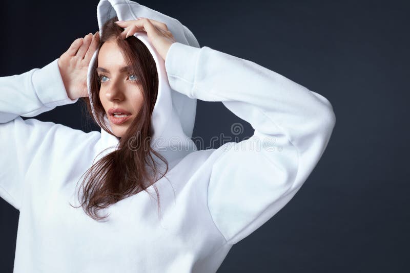 Stylish Girl. Beautiful Woman Close Up Portrait. Sensual Brunette Touching Head. Pretty Model In White Hoodie On Black Background