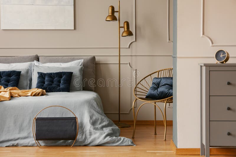 Stylish golden lamp next to king size bed with blue bedding and dark blue pillows