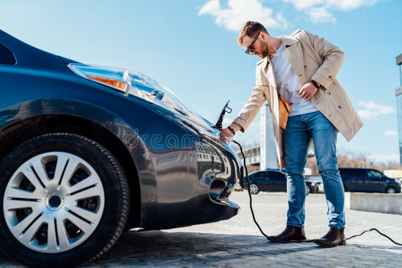 Stylish man in sunglasses disconnects the charging cable from his electric car.