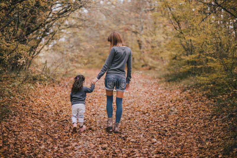 Mother and daughter walking in autumn forest holding hands. 
