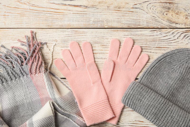 Stylish pink woolen gloves, scarf and hat on white wooden table, flat lay