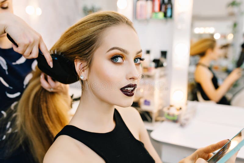 Stylish portrait of attractive young woman in beauty salon preparing to party. Making hairstyle, makeup, stylist