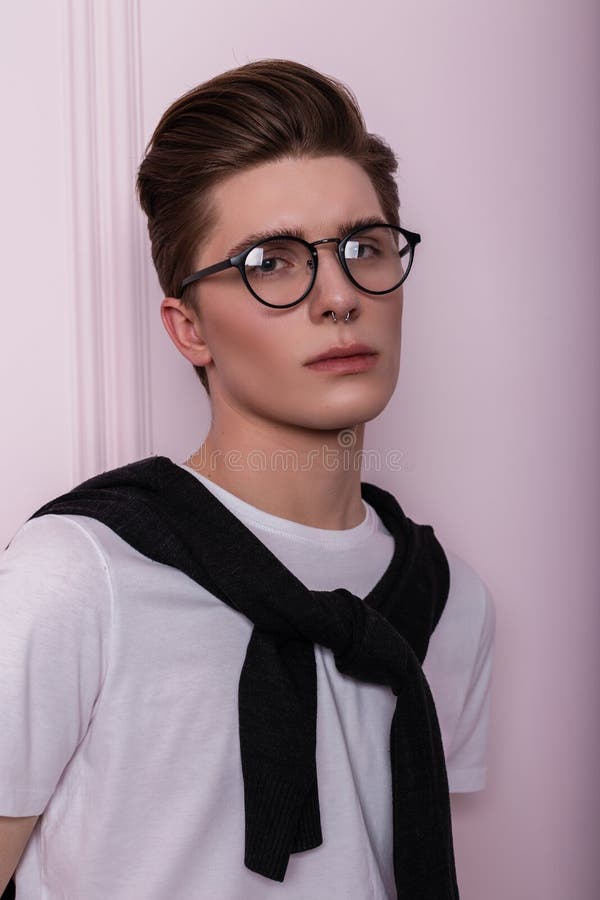 Stylish studio portrait of a handsome young hipster man with clean healthy skin in trendy glasses with nose piercing in a white T-