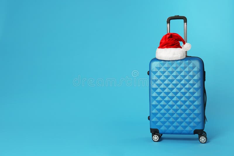 Stylish suitcase with Santa Claus hat on background, space for text. Christmas vacation