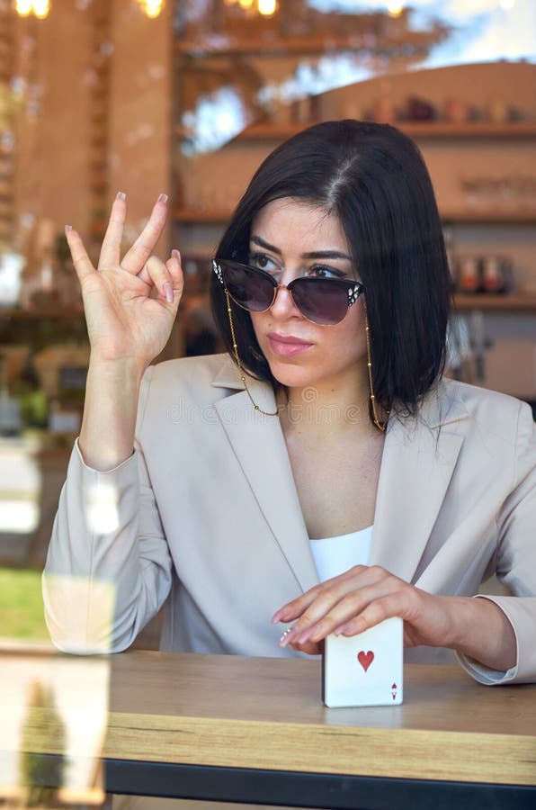 Stylish woman with a long manicure, fashionable sunglasses and a colored jacket through the glass of a cafe. royalty free stock photos Stylish woman with a long manicure, fashionable sunglasses and a colored jacket through the glass of a cafe. royalty free stock photos