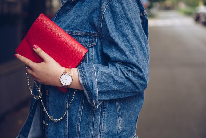 Stylish woman in polka dot culottes and denim jacket holding a red purse and wearing a rose gold wrist watch.