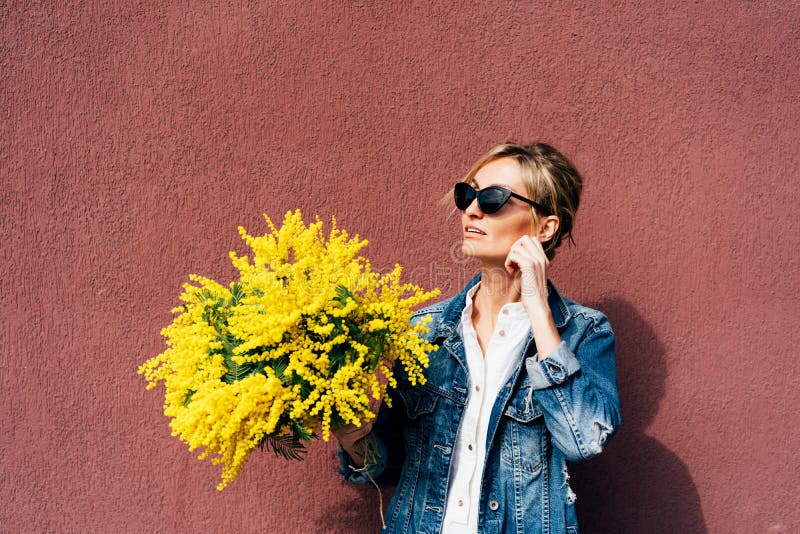 Stylish woman in sunglasses holds a bouquet of yellow mimosa flowers