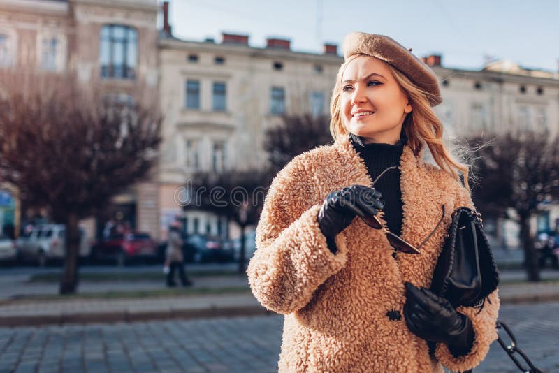 Stylish woman wearing teddy coat beret holding purse on city street. Autumn fashion female accessories and clothes