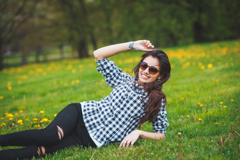 Stylish young girl in a plaid shirt and sunglasses lying on green grass in the spring