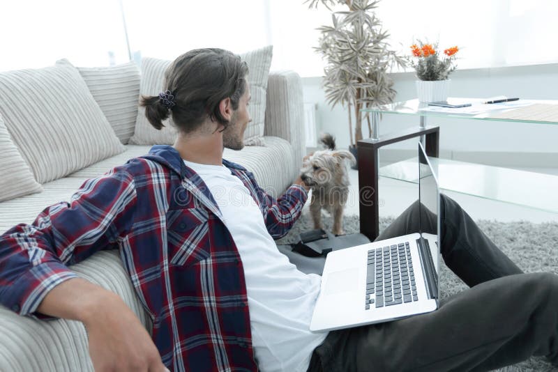 Stylish young man stroking his pet and working on laptop