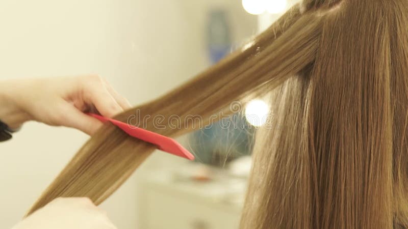 Styliste en coiffure peignant de longs cheveux et se redressant avec des pinces de cheveux dans le salon de coiffure Fermez-vous clips vidéos