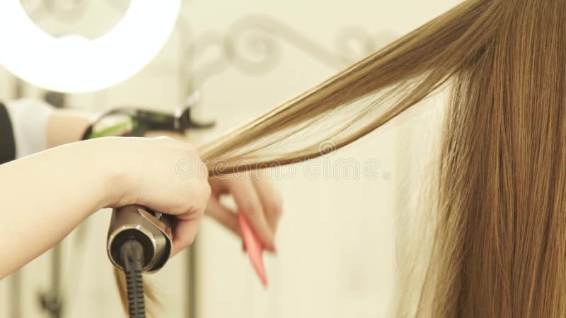 Styliste en coiffure à l'aide des pinces et du peigne de cheveux pour le hairstyling dans le salon de beauté Fermez-vous vers le clips vidéos