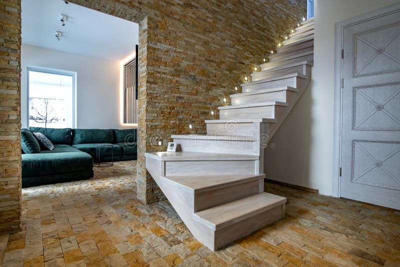 Stylish wooden contemporary staircase inside loft house interior. Modern hallway with decorative limestone brick walls and white oak stairs. Stylish wooden contemporary staircase inside loft house interior. Modern hallway with decorative limestone brick walls and white oak stairs.