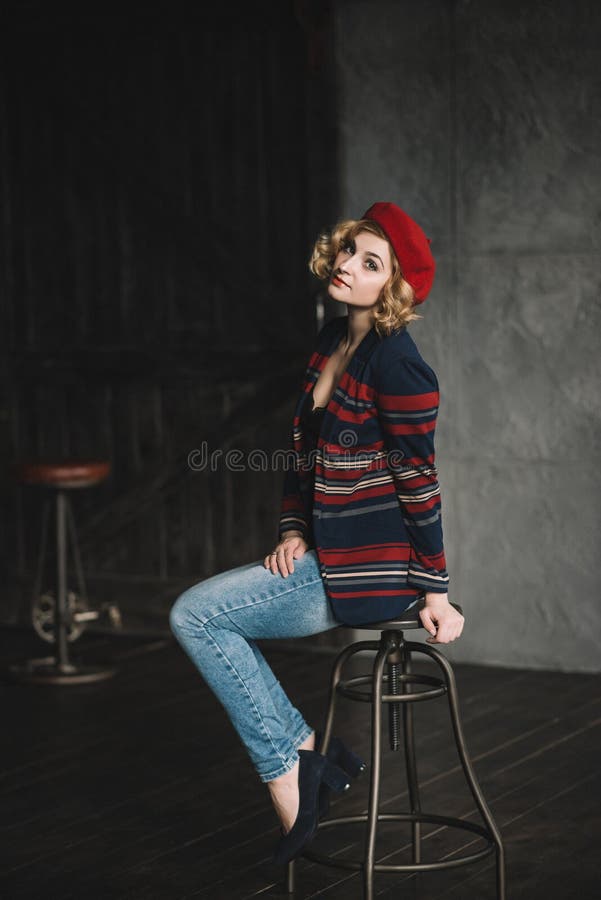 Stylish beautiful blonde girl in a red beret on a chair in a room in the loft style. Stylish beautiful blonde girl in a red beret on a chair in a room in the loft style..