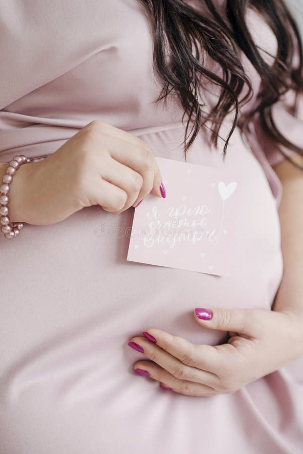 Stäng en gravid flicka i en rosa klänning och håll ett kort med inskriften royaltyfria foton Stäng en gravid flicka i en rosa klänning och håll ett kort med inskriften royaltyfria foton