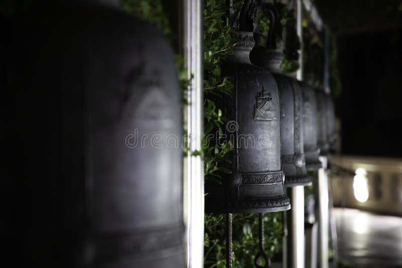Stäng sig upp av arrangera i rak linje järnklockor i en thai tempel på natten arkivfoton Stäng sig upp av arrangera i rak linje järnklockor i en thai tempel på natten arkivfoton