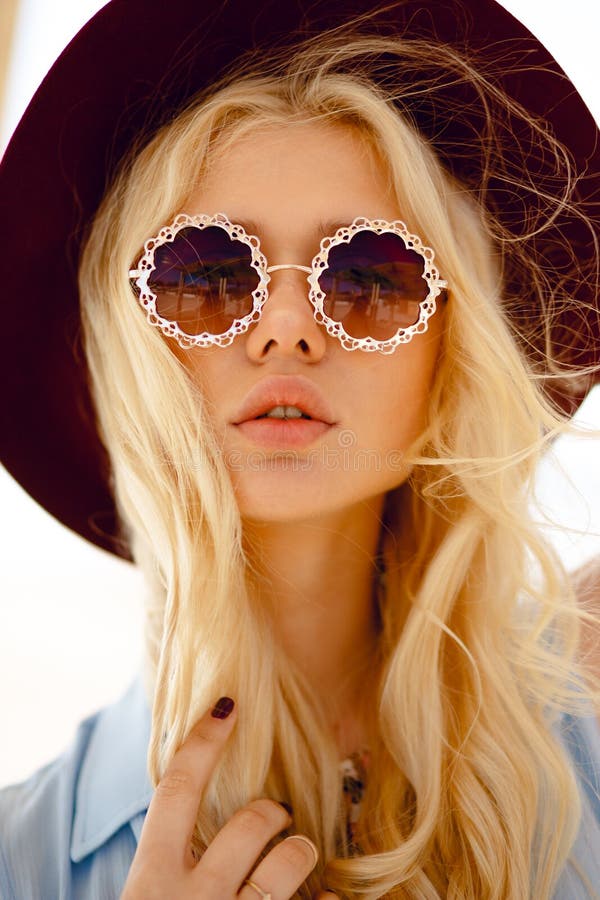St?ng sig upp av en sinnlig blondin med rund blom- solglas?gon, stora kanter, krabbt h?r och den burgundy hatten som ser kameran royaltyfri fotografi St?ng sig upp av en sinnlig blondin med rund blom- solglas?gon, stora kanter, krabbt h?r och den burgundy hatten som ser kameran royaltyfri fotografi