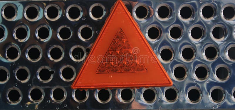 Stäng sig upp av ett skinande raster för metall med en reflekterande varnande triangel för orange ljus fotografering för bildbyråer Stäng sig upp av ett skinande raster för metall med en reflekterande varnande triangel för orange ljus fotografering för bildbyråer