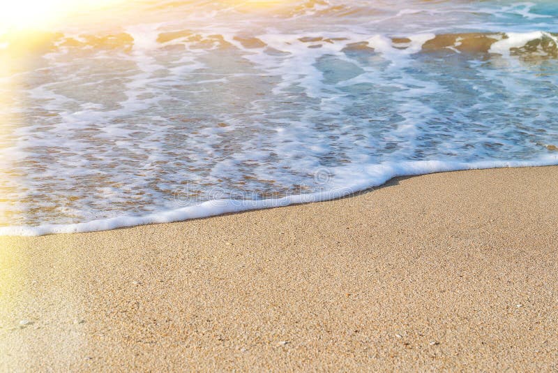 Stäng sig upp av ett skum för det vita havet på en gul kust- sand på en solig dag Marin- bakgrund med solfacklan arkivfoto Stäng sig upp av ett skum för det vita havet på en gul kust- sand på en solig dag Marin- bakgrund med solfacklan arkivfoto