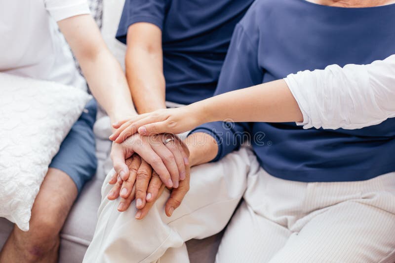 Stäng sig upp av familjen med vuxna barn och pensionärföräldrar som sätter händer som tillsammans hemma sitter på soffan tillsamm arkivbild