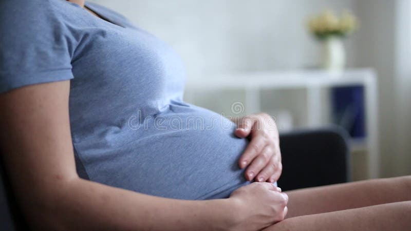 Stäng sig upp av gravid kvinnasammanträde på en soffa och att trycka på hennes mage lager videofilmer