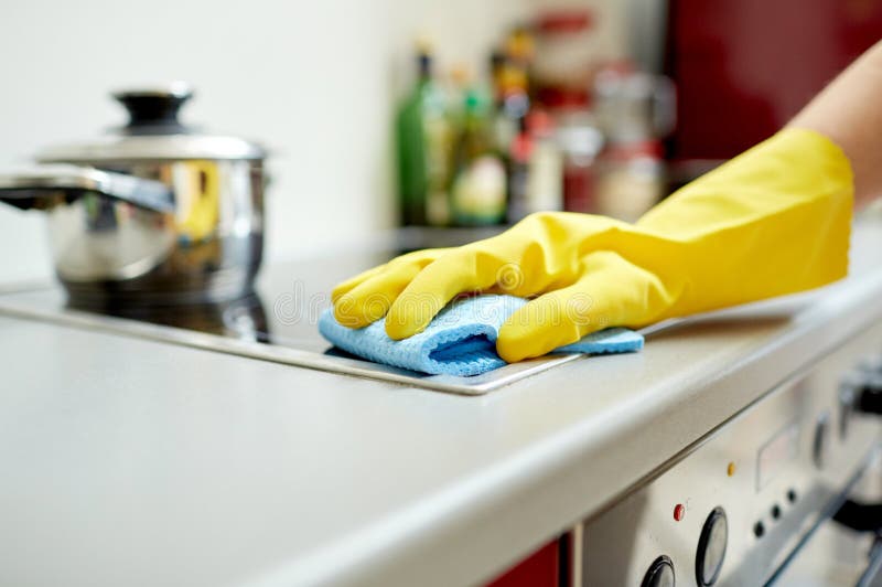 People, housework and housekeeping concept - close up of woman hand in protective glove with rag cleaning cooker at home kitchen. People, housework and housekeeping concept - close up of woman hand in protective glove with rag cleaning cooker at home kitchen