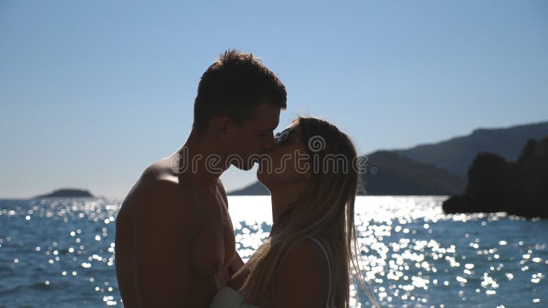 Stäng sig upp av härliga par som kysser nära kusten med solljusreflexion på vattenyttersidan på bakgrund Barn