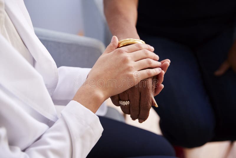 Stäng sig upp av kvinnlig hög kvinnapatient för doktor In Office Reassuring och att rymma hennes händer royaltyfri fotografi Stäng sig upp av kvinnlig hög kvinnapatient för doktor In Office Reassuring och att rymma hennes händer royaltyfri fotografi