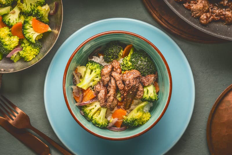 Stäng sig upp av sunt allsidigt näringmål i bunke med nötköttkött, ris, ångade grönsaker: broccoli och morötter som tjänas som me