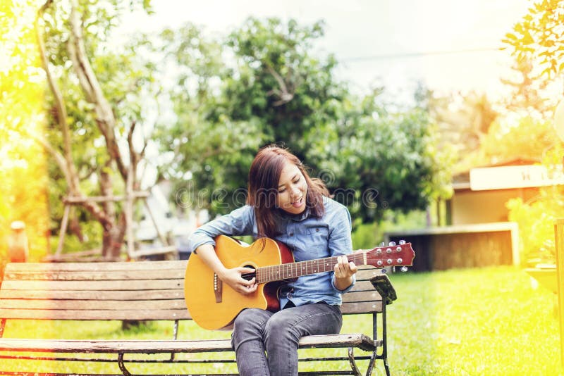 Stäng sig upp av ung hipster som kvinnan öva gitarren i parkerar, lyckligt och tyck om att spela gitarren arkivbild Stäng sig upp av ung hipster som kvinnan öva gitarren i parkerar, lyckligt och tyck om att spela gitarren arkivbild