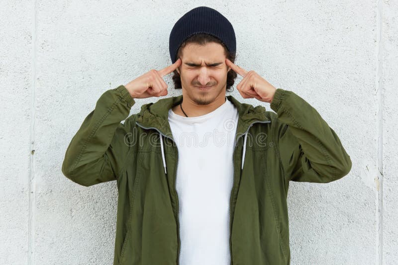 Stänger sig känner håller bär gör grön den stressiga tonårs- pojken för horisontalskottet ja, tryck, båda pekfingrar på tempel, d royaltyfri foto Stänger sig känner håller bär gör grön den stressiga tonårs- pojken för horisontalskottet ja, tryck, båda pekfingrar på tempel, d royaltyfri foto