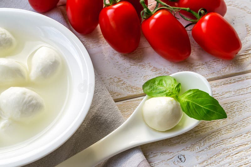 Stängning av en mini mozzarella-ostboll och en bäcken i en vit porslinssked nära en gren av röda körsbärstomater Healhy royaltyfri foto Stängning av en mini mozzarella-ostboll och en bäcken i en vit porslinssked nära en gren av röda körsbärstomater Healhy royaltyfri foto