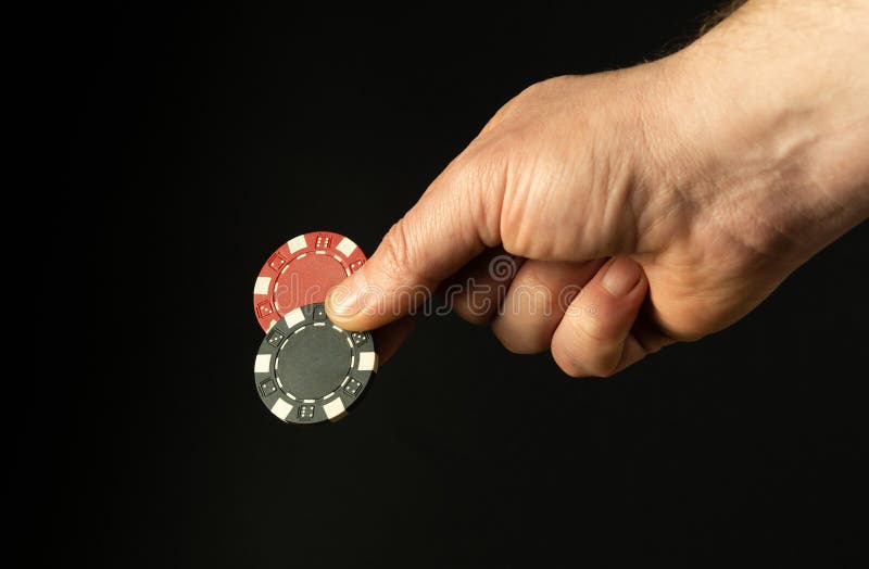 Close-up of a person's hand with two poker chips while betting to win. Free space for advertising on a black background. Close-up of a person's hand with two poker chips while betting to win. Free space for advertising on a black background.