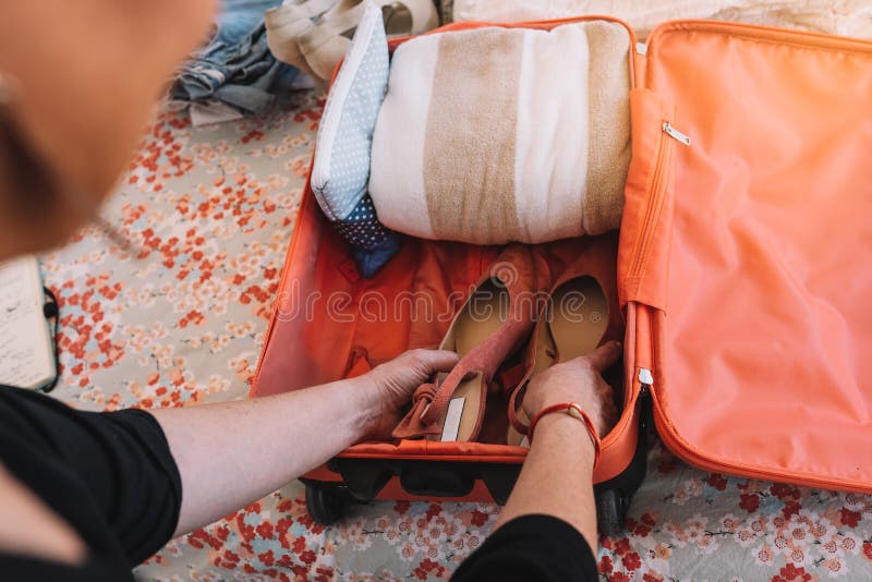 close-up of a suitcase being packed for a summer holiday. a woman& x27;s hands placing shoes in her luggage. travel and holiday concept. natural light, interior of a bedroom. close-up of a suitcase being packed for a summer holiday. a woman& x27;s hands placing shoes in her luggage. travel and holiday concept. natural light, interior of a bedroom.