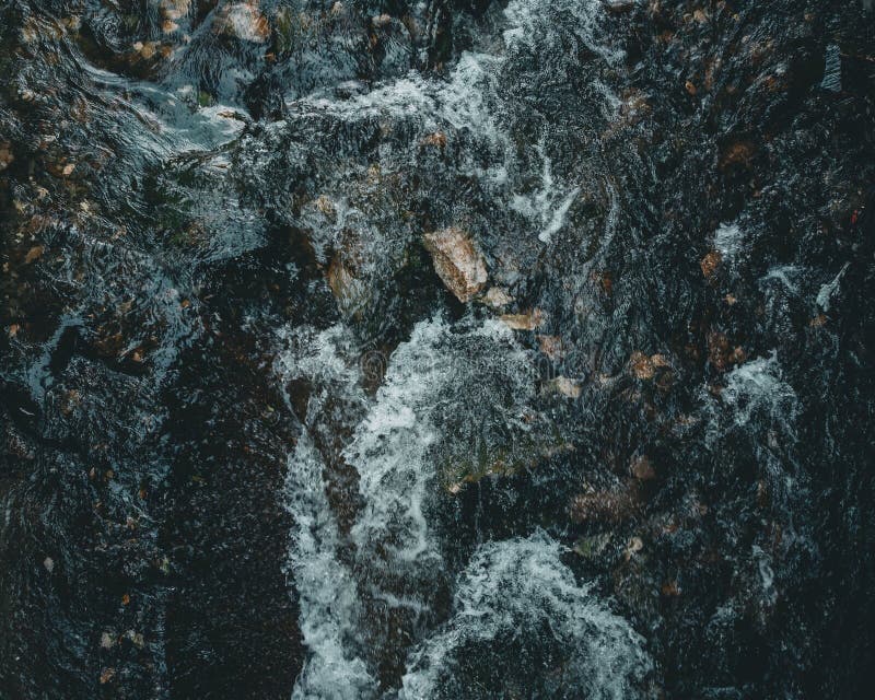 Stängning av en turbulent flod eller ström med snurrande skumvatten över mörka taggiga berg arkivfoto