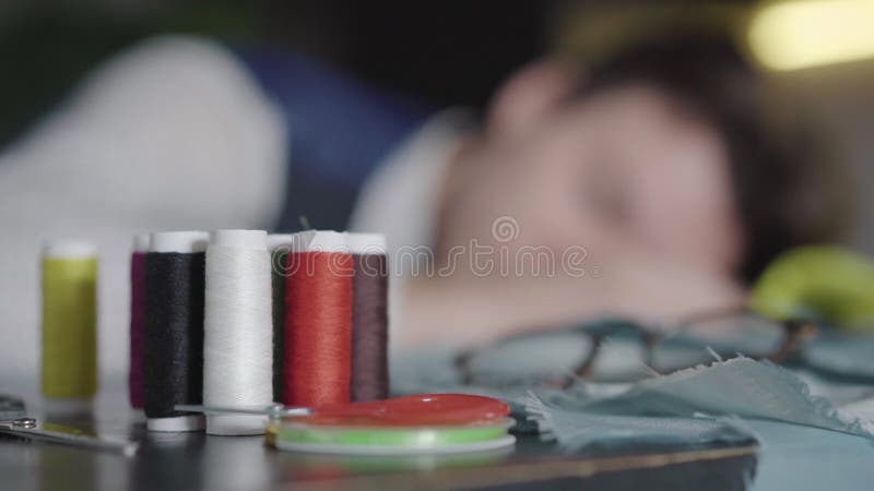 Stängning av flerfärgade sytråd med suddig designer som sover i bakgrunden. ung uttömd kaukasisk